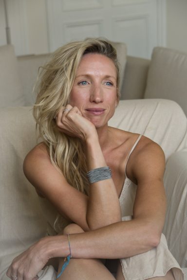 Vrouw met lang blond haar, zittend op een bank en nadenkend.
