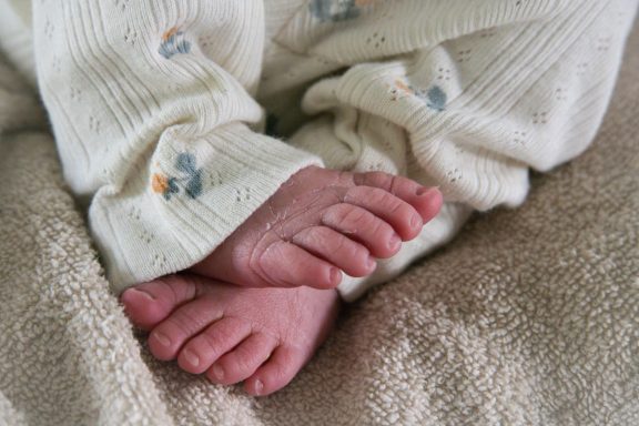 Een close-up van de voetjes van een baby, gekleed in een lichtkleurige romper.